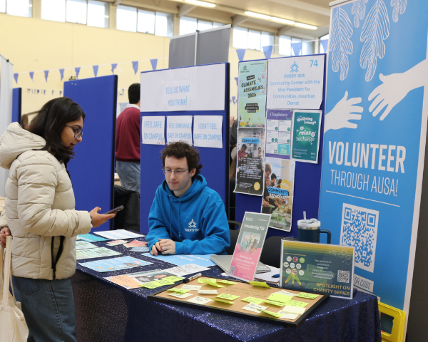 The volunteer at AUSA desk at the Welcome Fayre with interested students speaking to a staff member