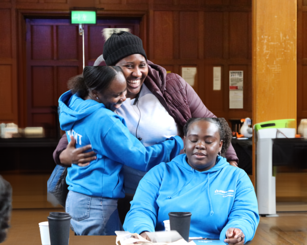 Two female class reps hug each other in the background while another female class reps is seated at a round table